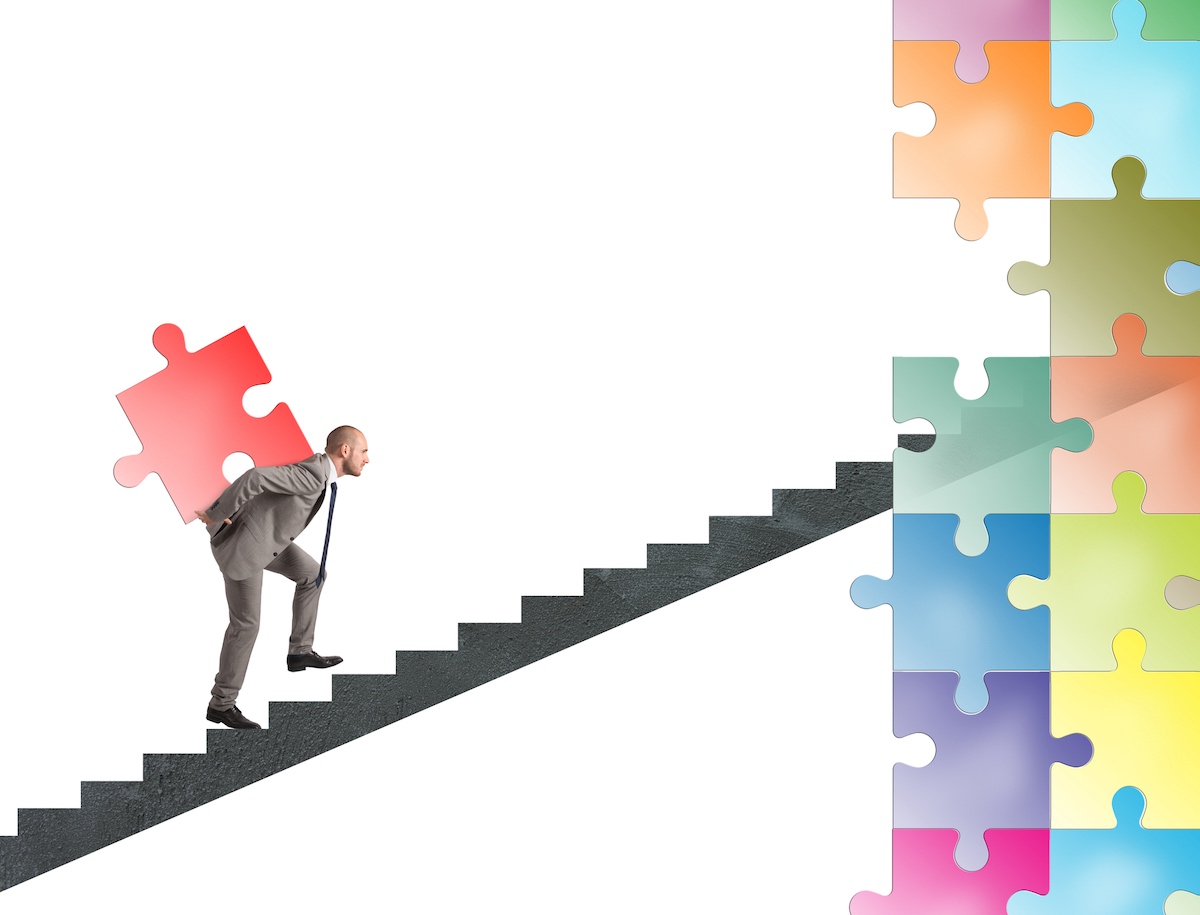 Why Hire a M&A Due Diligence and Integration Specialist Man climbing steps with puzzle piece on his back inferring he's helping a company with due diligence and integration in a merger and acquisition.